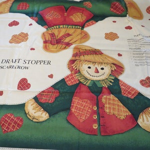 May include: A white fabric panel with a green, red, and yellow scarecrow design. The panel has the text "DOOR DRAFT STOPPER SCARECROW" and instructions for making a door draft stopper.