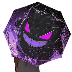 Puede incluir: Un paraguas morado y negro con un gráfico de un Pokémon fantasma con ojos rosados brillantes.