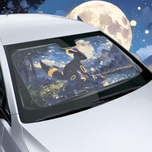May include: A car sunshade displaying a black Umbreon character with yellow details, set against a night scene with a full moon and mountains. The sunshade is designed to fit a car's windscreen.