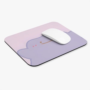 May include: A rectangular mousepad with a cartoon character design. The mousepad features a light purple character with a smiling face on a pink and purple background. A white wireless mouse rests on the pad.