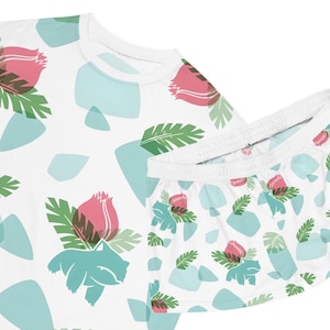 May include: White pajama set featuring a repeating pattern of pink flowers, green leaves, and blue geometric shapes. The set includes a short-sleeved top and matching shorts. The design is printed on a soft, lightweight fabric.