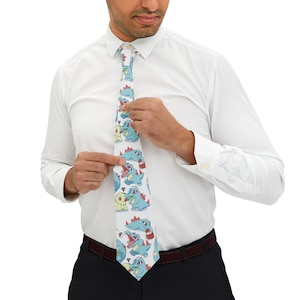 May include: A white necktie featuring a repeating pattern of light blue and pale yellow cartoon creatures with red spikes, small dark eyes, and open mouths, interspersed with small red and white circular icons on a clean white background.