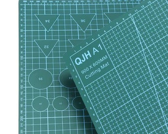 May include: A green cutting mat with white grid lines, numbers, and shapes. The mat has the text "QJH A 1" and "900 x 600mm Cutting Mat". The measurements are approximately 35.4 x 23.6 inches.