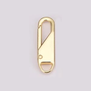 May include: A gold-colored metal clasp with a rectangular body and a curved top. The clasp has a small hole near the bottom and a loop at the base. The design is simple and functional, suitable for various applications.