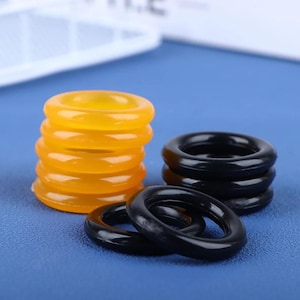 May include: A stack of five translucent yellow circular rings and a separate stack of three opaque black circular rings, with two additional black rings lying flat in the foreground, all featuring a smooth, rounded, and uniform circular shape.