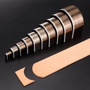 Puede incluir: Un conjunto de herramientas de artesanía en cuero metálico dispuestas en orden descendente de tamaño. Las herramientas están etiquetadas con texto y se utilizan para cortar cuero. Una pieza de cuero marrón claro está junto a las herramientas, con un trozo de cuero cortado.