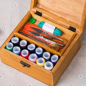 May include: A wooden sewing box with a hinged lid containing twelve spools of thread in various colors, a pair of silver metal scissors, a green measuring tape, and a gold-toned metal thimble arranged in a partitioned interior compartment.