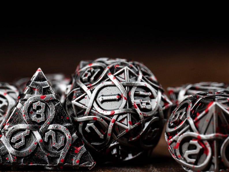 May include: Close-up of a set of metallic dice with intricate designs and red accents. The dice include a pyramid, a sphere, and other geometric shapes, ideal for tabletop gaming. The numbers are clearly visible.