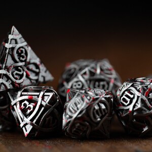 May include: A collection of intricately designed dice in various shapes, including a pyramid and a sphere. The dice are primarily silver with black accents and red highlights, creating a striking contrast. The numbers are clearly visible.