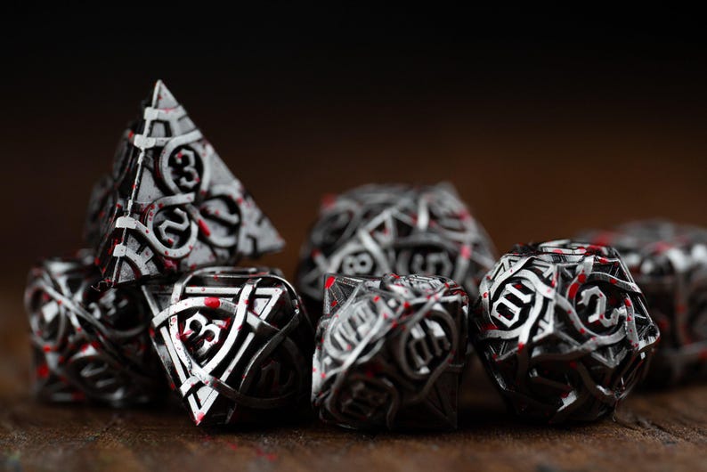 May include: A collection of intricately designed dice in various shapes, including a pyramid and a sphere. The dice are primarily silver with black accents and red highlights, creating a striking contrast. The numbers are clearly visible.
