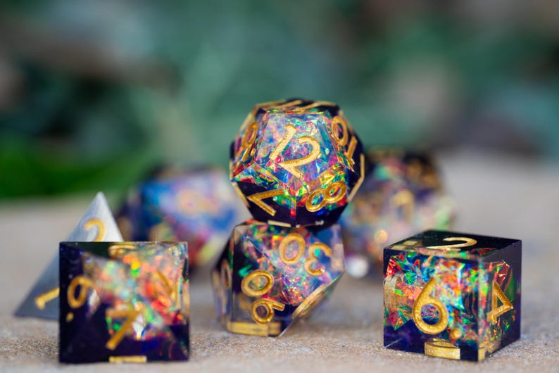 May include: A collection of polyhedral dice with a dark blue base and gold numbering. The dice are filled with colorful, iridescent glitter, creating a shimmering effect. The set includes various shapes, such as a d20, d6, and d4, perfect for tabletop gaming.
