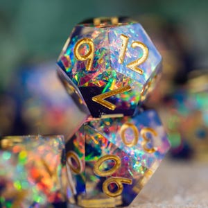 May include: Close-up of several polyhedral dice with a shimmering, iridescent interior. The dice have gold-colored numbers and edges. The dice are primarily blue with colorful glitter and are designed for tabletop gaming.
