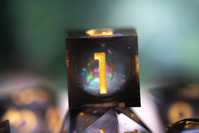 May include: A black and clear resin dice with gold glitter and a gold number "1" on one side.