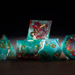 May include: A collection of polyhedral dice in various shapes. The dice are teal and clear with gold numbering and red accents. The dice are arranged on a dark surface, with a shallow depth of field.