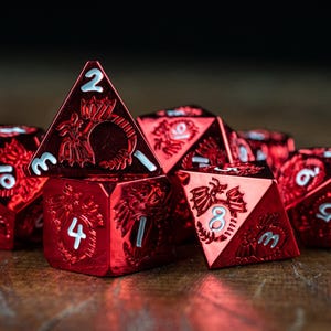 May include: A collection of red metallic polyhedral dice with white numbering and dragon-themed engravings. The dice are arranged on a wooden surface, showcasing their multifaceted shapes and intricate designs, perfect for tabletop gaming.