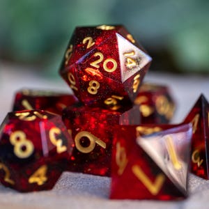 以下が含まれることがあります： 赤と金の様々な形と数字のサイコロのセット。サイコロは、赤と金のキラキラ効果のある透明なプラスチック製です。