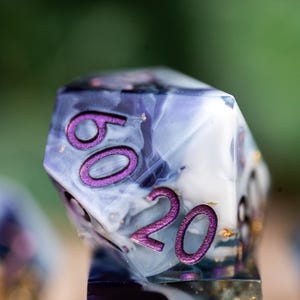 May include: A close-up of a purple and white dice with gold flecks. The dice has the numbers 60 and 20 on it.