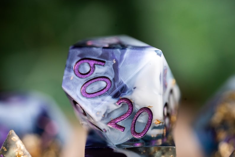 May include: A close-up of a purple and white dice with gold flecks. The dice has the numbers 60 and 20 on it.