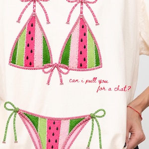 May include: An off-white t-shirt featuring a graphic of a bikini with a watermelon pattern in shades of pink, light green, and dark green with black seeds. The text "can i pull you for a chat?" is printed in red cursive script next to the bikini top.