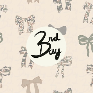 May include: A pattern of bows in various shades of green, brown, and tan, some with a camouflage design, against a light beige background. A white circle in the center features the text "3rd Day" in black script.