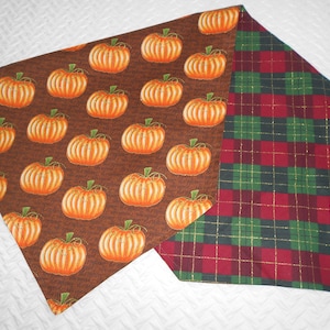 May include: A brown and orange table runner with a pumpkin pattern on one side and a red and green plaid pattern on the other side.