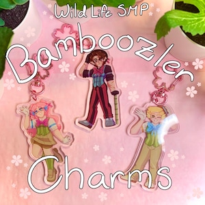 May include: Three acrylic charms featuring cartoon characters. The charms have a pink flower-shaped keychain attachment. The text "Bamboozler Charms" is written in a white, outlined font. The background is pink with white flower details.