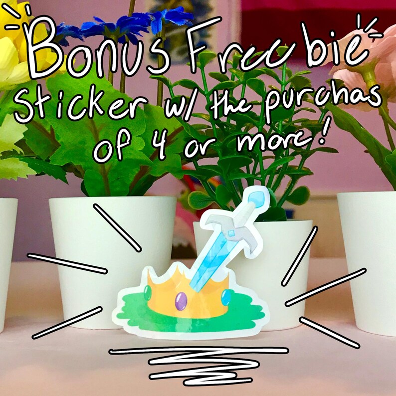 May include: A sticker of a gold crown with a blue sword sticking out of it. The sticker is on a white background with a pink wall in the background. The text "Bonus Freebie! Sticker w/ the purchase of 4 or more!" is written in yellow and black on the top of the image.