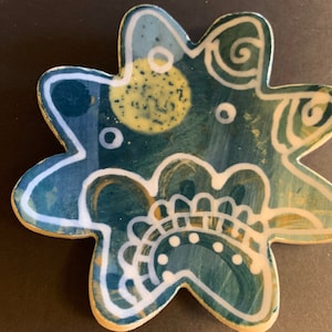Puede incluir: Un plato de cerámica azul y amarillo con forma de estrella y diseños pintados en blanco. El plato tiene una superficie texturizada y un acabado brillante.
