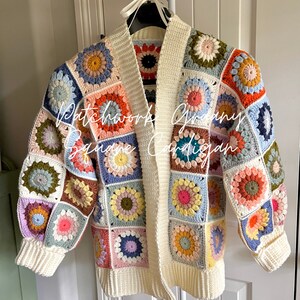 May include: A handmade, open-front cardigan featuring a patchwork design. The sweater is composed of colorful, crocheted granny squares in various pastel shades, with a cream-colored border and cuffs. The text "Patchwork Groovy Square Cardigan" is written on the front.