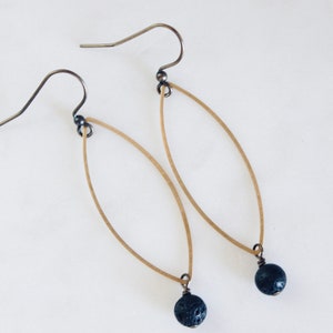 May include: A pair of gold oval earrings with black lava rock beads hanging from the bottom.
