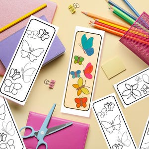 May include: A collection of butterfly-themed bookmarks. Some bookmarks feature black and white butterfly outlines, while others showcase colorful butterfly illustrations. Pencils, notebooks, and scissors are also visible, suggesting a school or craft theme.
