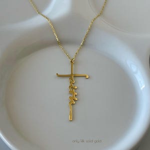 K&ouml;nnte beinhalten: Eine goldfarbene Halskette mit einem Kreuzanh&auml;nger. Das Wort "faith" ist in einer Schreibschrift in der Mitte des Kreuzes geschrieben. Die Halskette liegt auf einer wei&szlig;en Oberfl&auml;che. Der Text "only 14k solid gold" steht unten.