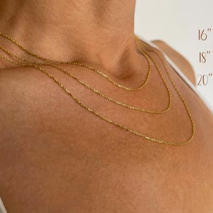 K&ouml;nnte beinhalten: Drei zarte goldene Halsketten in verschiedenen L&auml;ngen, 16, 18 und 20 Zoll (40,6, 45,7 und 50,8 cm), werden gezeigt. Die Ketten sind um den Hals einer Person drapiert und zeigen die verschiedenen L&auml;ngen. Die Halsketten haben ein schlichtes, elegantes Design.