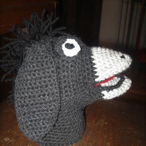 May include: A black crocheted donkey puppet with a white eye and a red mouth. The puppet has a gray crocheted nose and a black crocheted mane.