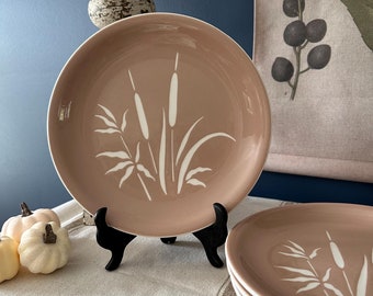 Pode incluir: Conjunto de quatro pratos de jantar cor-de-rosa com um design floral branco. Os pratos apresentam uma imagem estilizada de juncos e ervas.