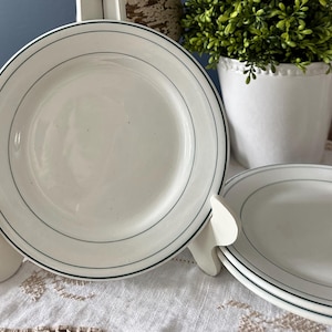 Puede incluir: Dos platos de cerámica blanca con un borde verde. Los platos tienen un diseño sencillo con una sola banda verde alrededor del borde.