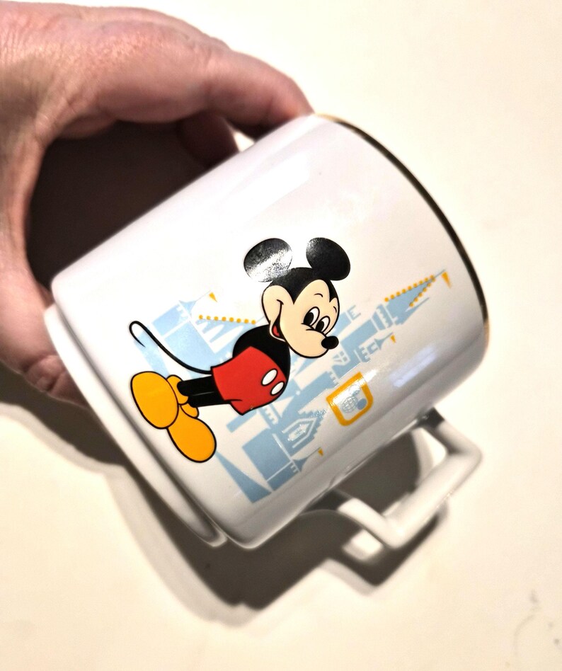 Puede incluir: Taza de cer&aacute;mica blanca con Mickey Mouse con su atuendo cl&aacute;sico, con un dise&ntilde;o de castillo azul claro. La taza tiene un borde dorado y un asa blanca. Un cl&aacute;sico de colecci&oacute;n de Disney.