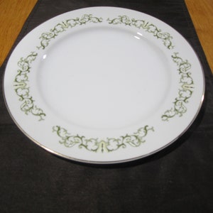 May include: A white ceramic dinner plate with a green and gold floral design around the rim.