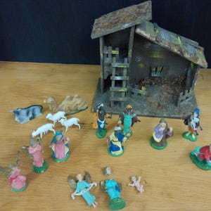 May include: A vintage Nativity scene set with a wooden stable, figurines of the Holy Family, angels, and the Three Wise Men. The figures are painted in various colors and arranged on a wooden surface.