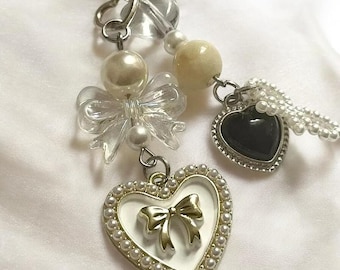 May include: A silver charm bracelet with a heart-shaped pendant, a clear crystal charm, a pearl charm, a white heart-shaped pendant with a gold bow, and a black heart-shaped pendant with a silver border.