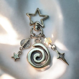 May include: A silver charm keychain with a star-shaped ring, a spiral charm, a pearl-like bead, and two star-shaped charms.