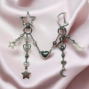 Pu&ograve; includere: Un braccialetto con ciondoli in argento a forma di stella, luna e cuore. I ciondoli sono collegati da una catena d'argento e hanno piccole perline e cristalli.