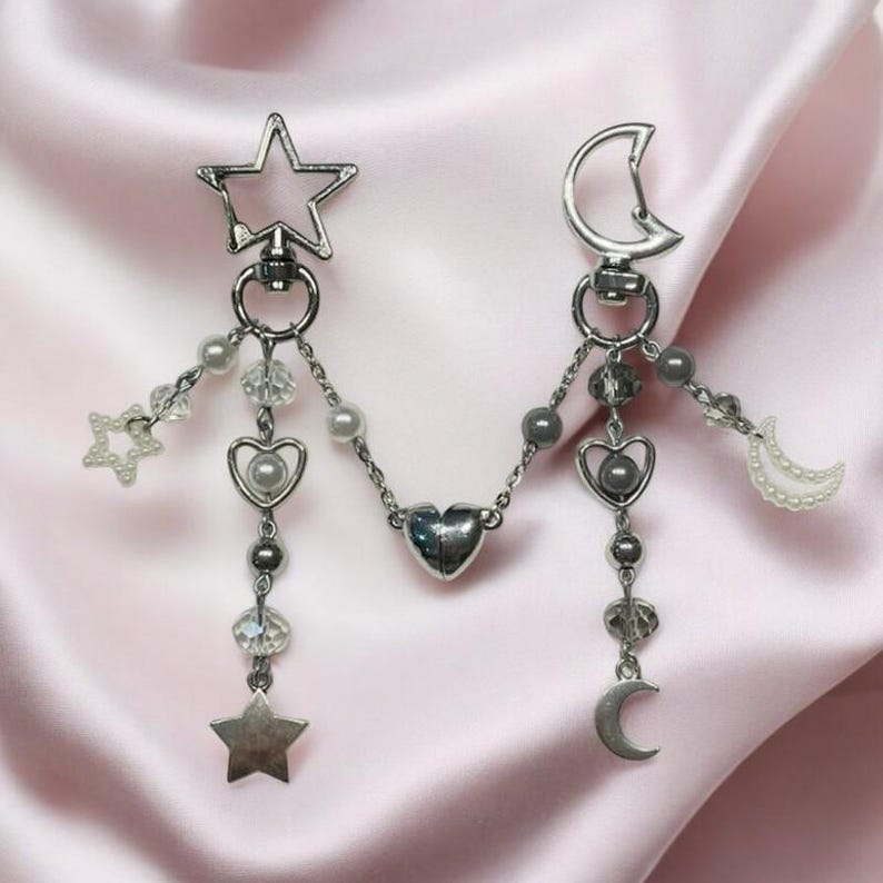 Pu&ograve; includere: Un braccialetto con ciondoli in argento a forma di stella, luna e cuore. I ciondoli sono collegati da una catena d'argento e hanno piccole perline e cristalli.