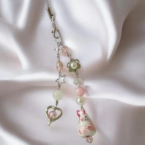 May include: A silver charm bracelet with pink and white beads, a heart charm, a star charm, a flower charm, and a small ceramic bunny charm.