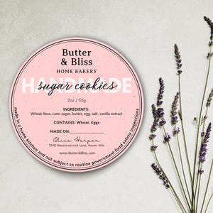 Può includere: Un'etichetta circolare rosa per "Butter & Bliss Home Bakery" con il testo "Handmade Sugar Cookies". L'etichetta include ingredienti e informazioni di contatto. Rametti di lavanda sono sul lato destro dell'immagine.