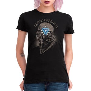 May include: Black t-shirt featuring a graphic of a skull wearing a respirator with a blue and white triangle design. The text "BLACK SABBATH" is arched above the skull. The shirt is a classic crew neck style.