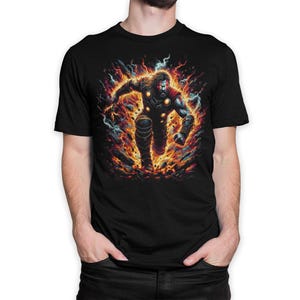 May include: A black short-sleeved t-shirt featuring a graphic print of a muscular, bearded warrior figure in dark armour, surrounded by vibrant orange and yellow flames, glowing embers, and streaks of blue lightning, set against a solid black background.