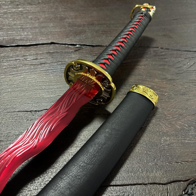 May include: A decorative katana sword with a red blade and black handle. The handle is wrapped with red stitching. The guard and pommel are gold-colored with intricate designs. The scabbard is black with a gold-colored cap.