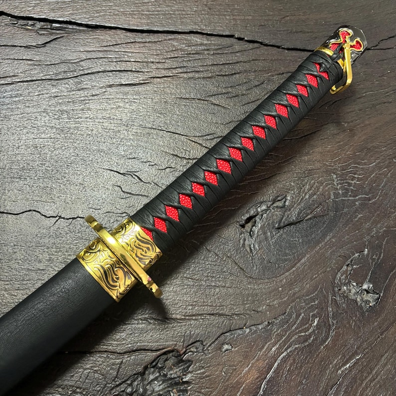 May include: A black katana sword with a red diamond pattern on the handle. The sword features gold-colored accents on the guard and pommel, and is set against a dark wood background.