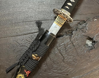 May include: A Japanese katana sword with a black handle and scabbard. The scabbard features a gold dragon design with red accents. The blade is partially visible, and the hilt has intricate gold detailing.